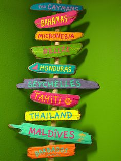 there are many different colored wooden signs on the pole in front of a green wall