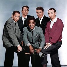 four men in suits and ties posing for a photo with one sitting on a chair