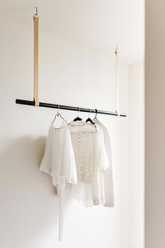 three shirts hanging on a clothes rail in a room with white walls and wooden flooring