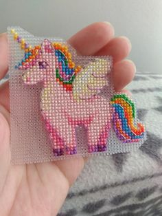 a hand holding a small cross stitch unicorn brooch