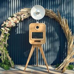 a wooden tripod with a white radio on top and a flower wreath around it