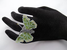 a hand with a green butterfly brooch sitting on it's palm next to a black glove