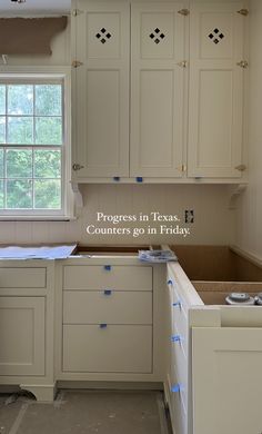 an empty kitchen with white cabinets and blue tape on the counter tops that says progress in times counters go in friday