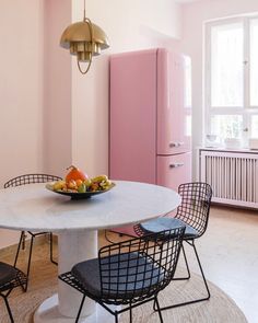 a bowl of fruit sits on a table in the middle of a room with pink walls