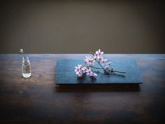 a wooden table with a bottle and flowers on it, next to a small flower vase