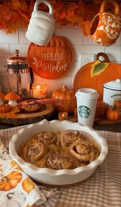 a table topped with pumpkin pies next to a white plate filled with cinnamon rolls