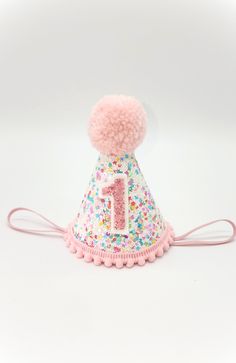 a pink and white hat with a number one on the top, decorated with sprinkles