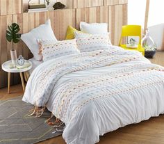 a bed with white comforter and pillows in a room next to a yellow chair