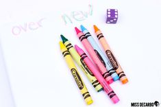 three crayons and two dice on top of a notepad with the words over new