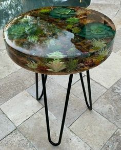 a glass table with plants on it sitting in the middle of a patio area next to a swimming pool