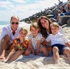 the family is sitting on the sand at the beach and posing for a photo together