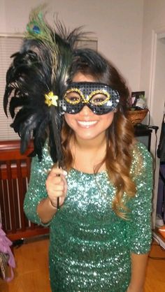 a woman in a green dress wearing a masquerade with feathers on her head