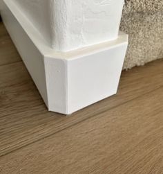 a close up view of the corner of a white base on a wood flooring