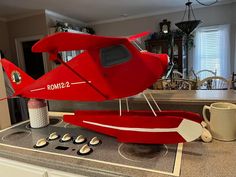 a red model airplane sitting on top of a kitchen counter next to a cup and coffee mug