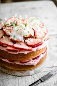 a cake with strawberries and white flowers on top is sitting on a wooden table