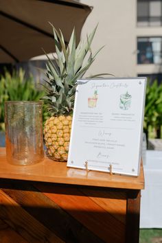 a pineapple sitting on top of a wooden table next to a glass and menu