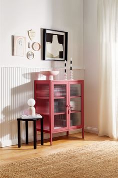 a red cabinet sitting on top of a hard wood floor next to a white wall