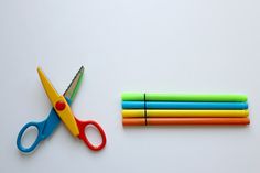 a pair of scissors next to colored pencils on a white surface with erasers