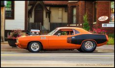 an orange and black muscle car parked on the side of the road in front of a house