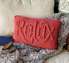 a crocheted pillow with the word love written on it sitting on a couch