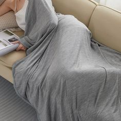 a woman laying on a couch with a blanket over her head and reading a magazine