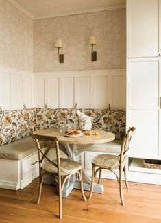 a corner table with two chairs and a bench in the middle of a room filled with white cupboards