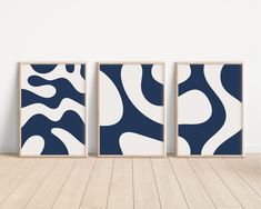 three blue and white art prints on a wall in an empty room with wood flooring