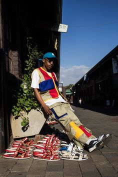 a man sitting on the ground next to many pairs of shoes and planter in front of him