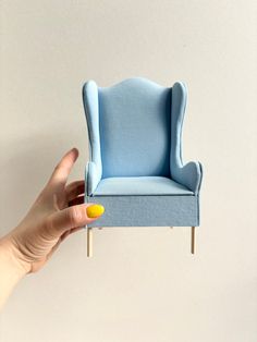 a miniature blue chair sitting on top of a wooden stick in someone's hand