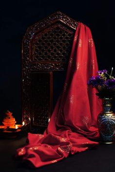 a vase with purple flowers sitting next to a red cloth on a black tablecloth