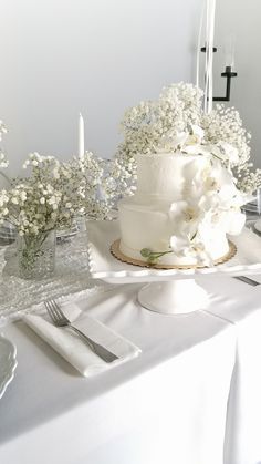 a white cake sitting on top of a table next to candles and flowers in vases