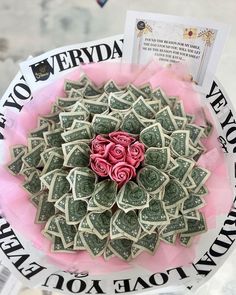 a bunch of money sitting on top of a pink paper plate with roses in it