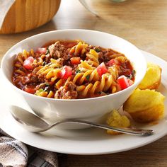 a white bowl filled with pasta and meat on top of a plate next to potato wedges