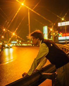 a man with a backpack leaning against a rail on the side of a road at night