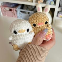 a person holding two small crocheted animals in their hands, one is white and the other is brown