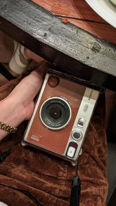 an old camera sitting on top of a brown blanket next to a person's hand