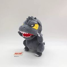 a small stuffed animal with yellow eyes and big teeth, sitting on a white surface