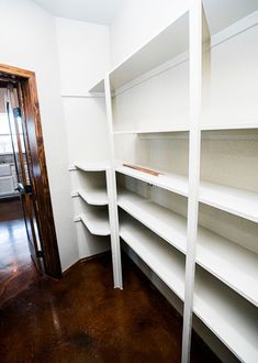 empty white shelves in the corner of a room next to a door and wooden floor