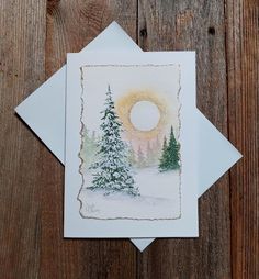 a greeting card featuring a snowy scene with trees and the sun in the distance, on a wooden background