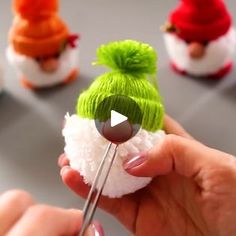 a person holding a pair of scissors in front of small knitted santa hats on top of cotton balls