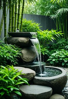 a water fountain in the middle of a garden with rocks and bamboo trees behind it