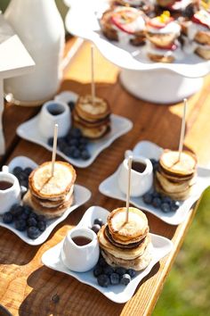 some pancakes and blueberries are on small plates with toothpicks in the middle