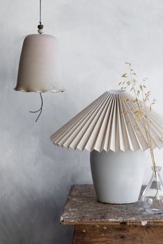 a white vase sitting on top of a wooden table next to a light fixture and lamp