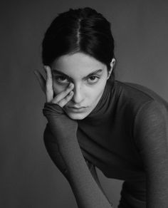 a black and white photo of a woman with her hand on her face, looking at the camera