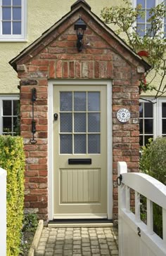 a small brick house with a white gate and clock on the front door is shown