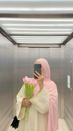 a woman taking a selfie with her cell phone in an elevator holding a bouquet of flowers