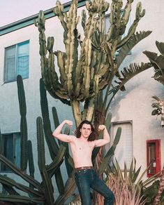 a shirtless man standing in front of a cactus tree with his arms stretched out