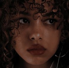 a close up of a person with curly hair and scissors in their hands, looking at the camera