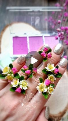 a woman's hand with pink and yellow flowers on her nails in front of a mirror