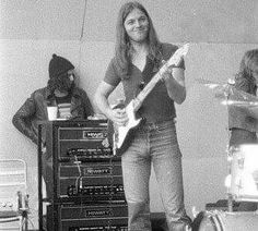 a man standing next to a stack of sound equipment in front of a guitar player